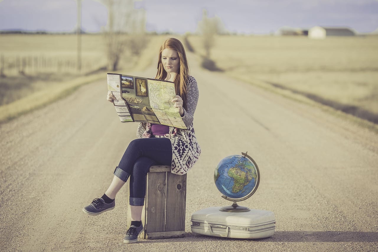 Woman seating on a suitcase reading a map on the side luggage and globs